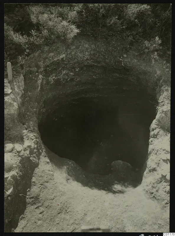 Excavated Tomb 13 at Marion: a dark opening cut into pale earth, with grass above and stones at the edges