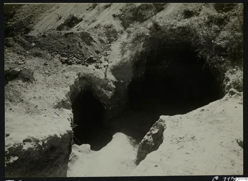 Excavated tomb entrances cut into a sandy slope at Marion, with a dark chamber opening beyond.