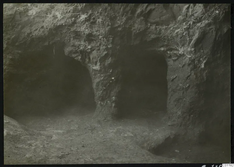 Tomb 9 at Marion: two dark arched openings cut into a rock face, with an earthen floor in front