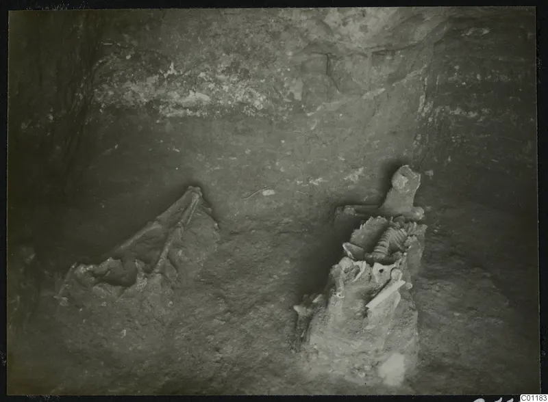 Tomb 9 at Marion during excavation, with a skeleton lying among stones in a rock-cut chamber