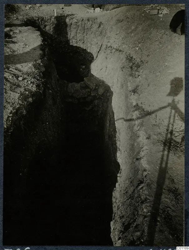 Tomb 26 at Marion during excavation, showing a deep narrow cut with a stone-edged opening in its side.