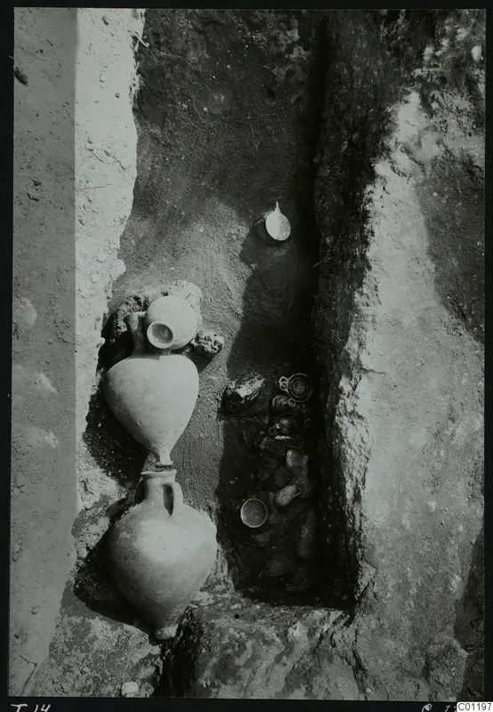 Tomb 14 at Marion during excavation, with pottery vessels standing and lying in a narrow cut in the earth.