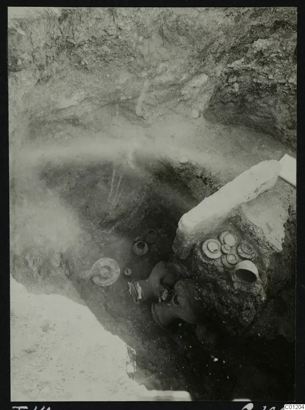 Tomb 14 at Marion during excavation, with pottery vessels and a large stone slab lying in the pit