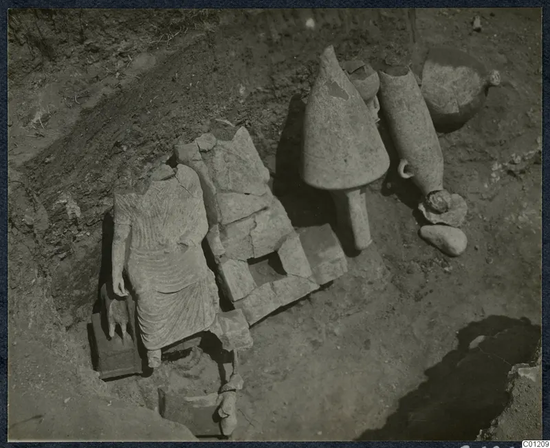 Tomb 30 at Marion: a headless draped stone statue and large stone vessels among stone fragments during excavation