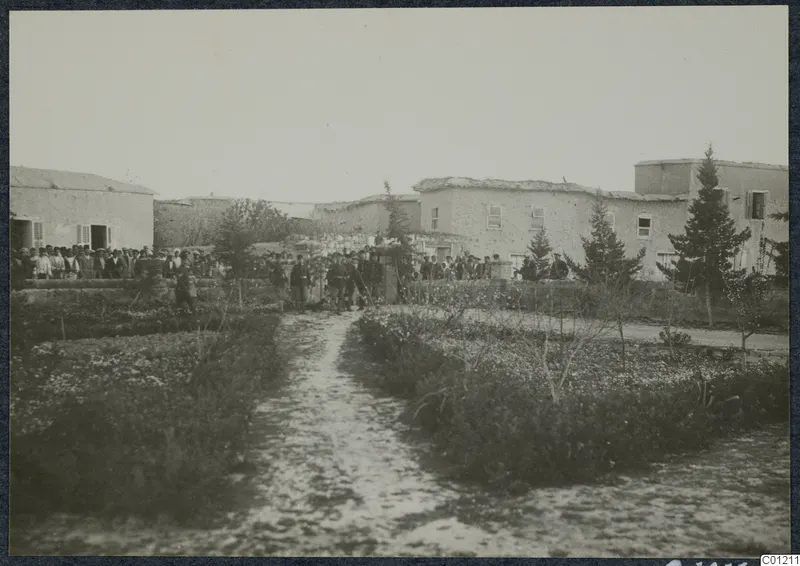 Crowd of people in dark clothing among whitewashed flat-roofed buildings and conifer trees at Marion.