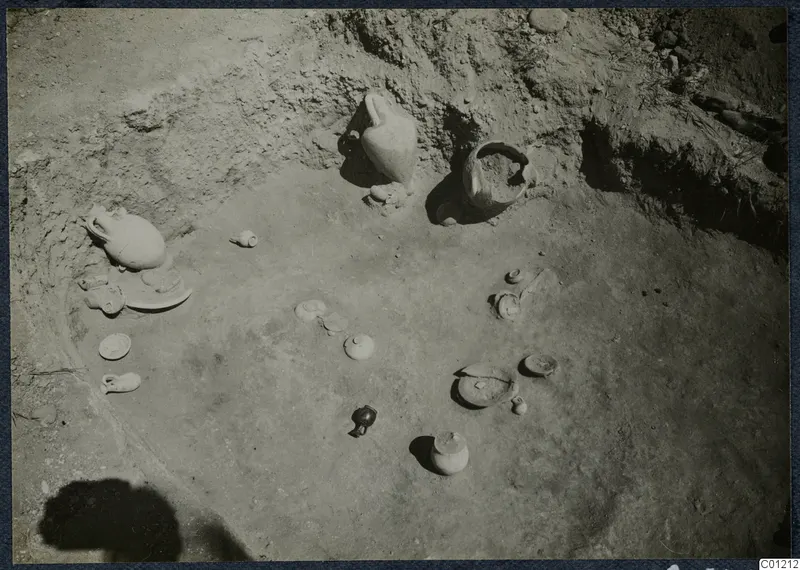 Excavated tomb floor at Marion with scattered pottery vessels, lids and small objects in situ.