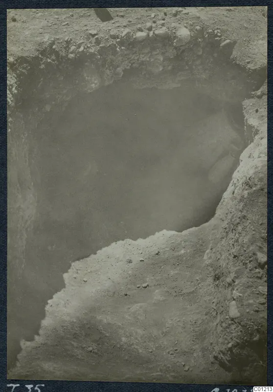 Excavation of Tomb 35 at Marion, with a dark cavity in the cut and stones along the upper edge.