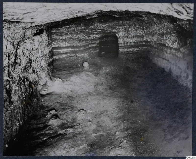 Interior of Tomb 36 at Marion, with small objects lying on the chamber floor and a niche in the back wall