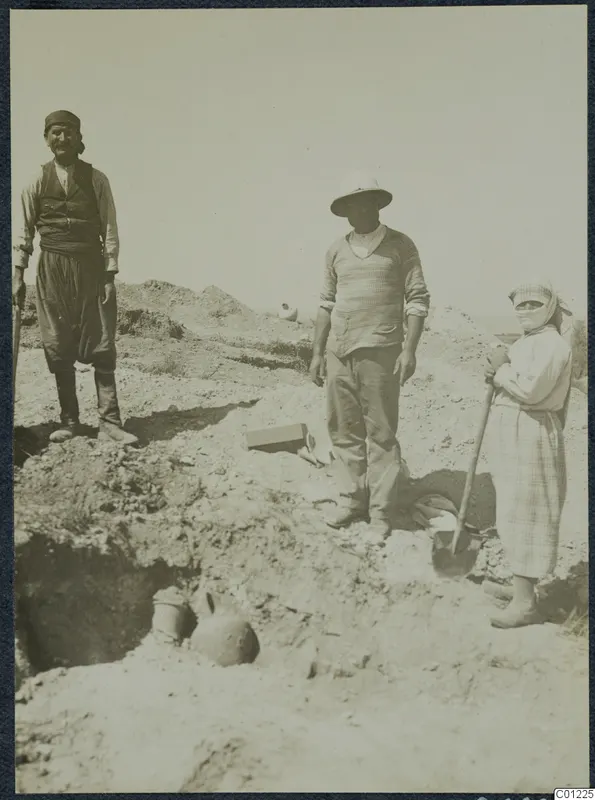 Three people standing in an excavation at Marion, with pottery vessels partly uncovered in the trench in front of them.