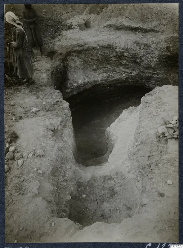 Tomb 38 at Marion during excavation, with a woman holding a tool beside an open cut leading to a dark tomb opening