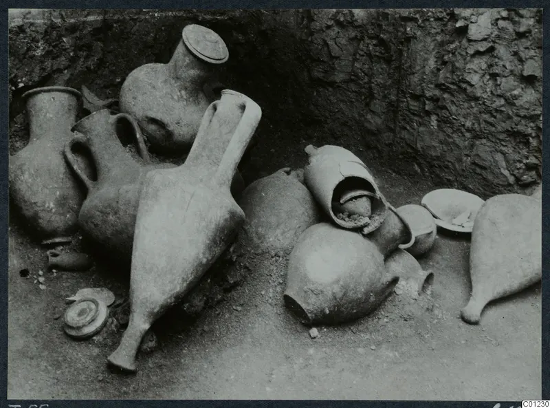 Pottery vessels lying in situ on the floor of Tomb 55 at Marion, against a rough rock-cut wall