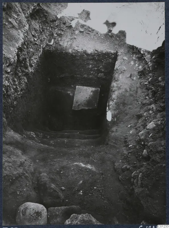 Tomb 53 at Marion during excavation, with steps leading up to a square stone slab in the back wall.