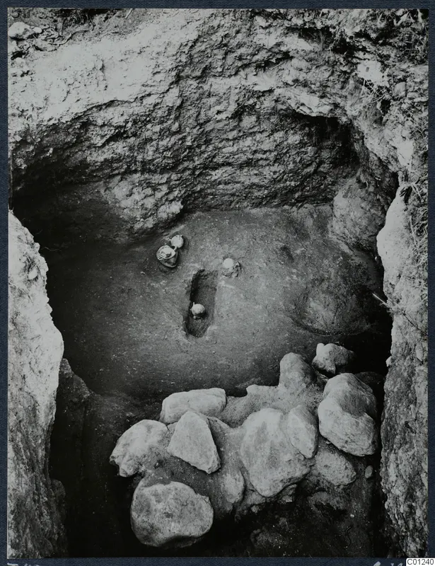 Tomb 49 at Marion during excavation, with vessels in the floor and a heap of stones across the front