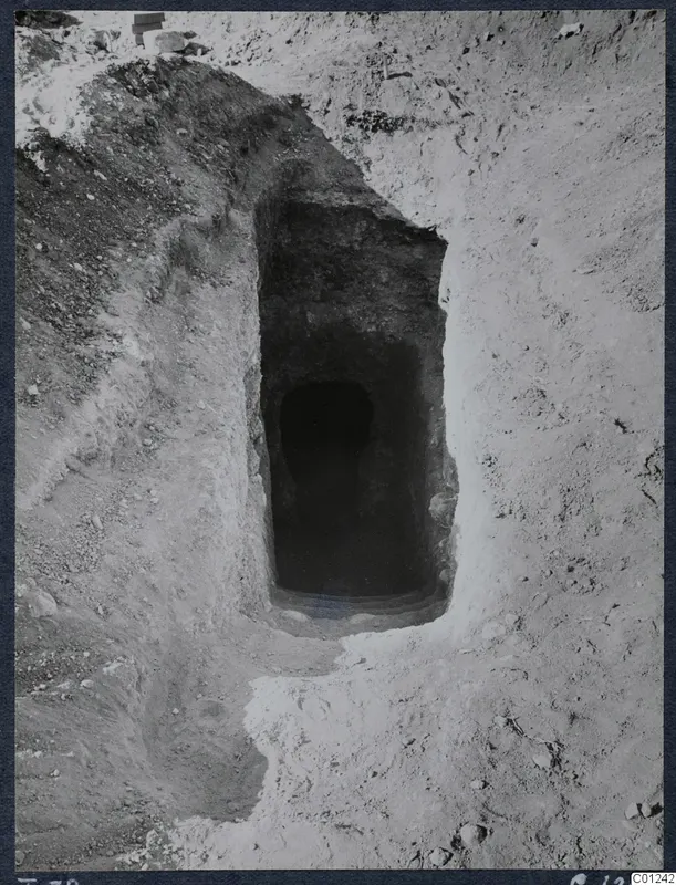 Tomb 39 at Marion: a sloping dromos leading down to the dark doorway of a tomb chamber in excavated ground.