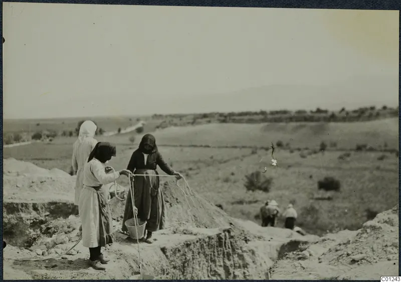 Women working at the edge of an excavation trench at Marion, one holding a rope above a bucket.