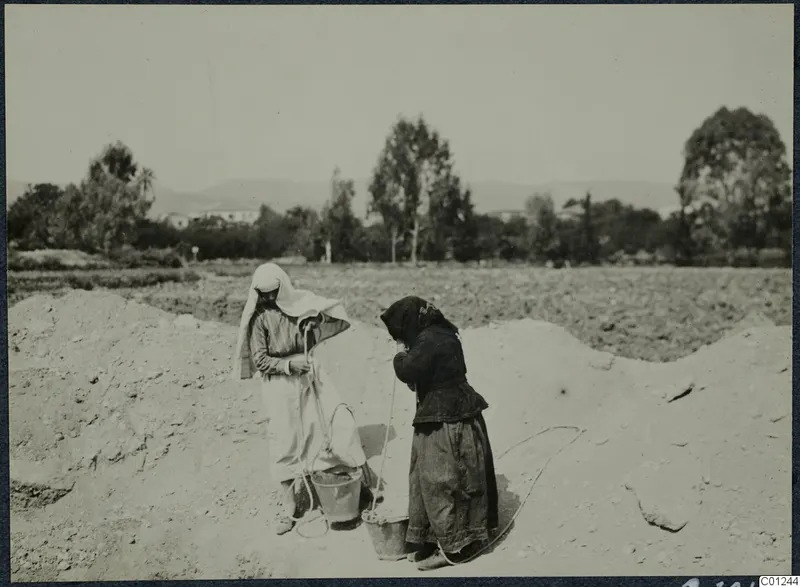 Two women with buckets working on a spoil heap at Marion, fields and trees behind them.