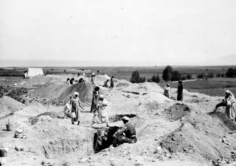 Many people working in trenches at the Marion excavation, with a white tent on the left under a wide sky
