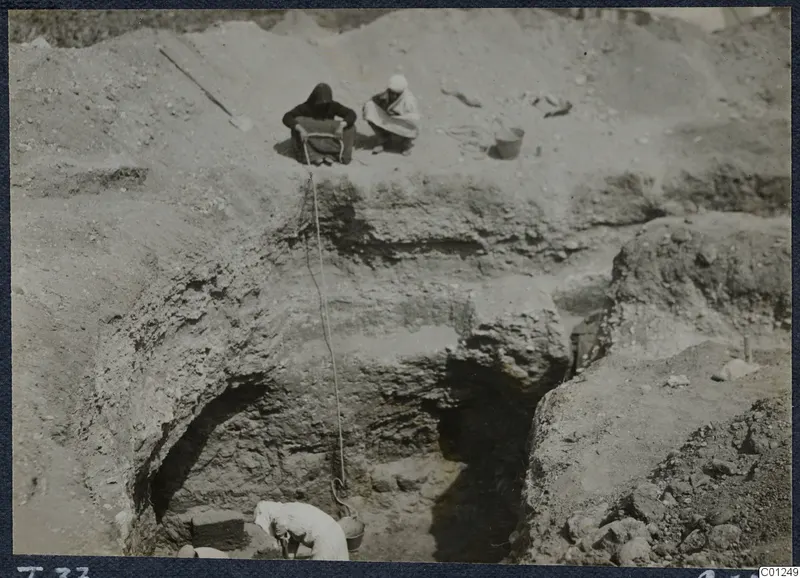 Excavation of Tomb 37 at Marion, with workers seated at the cut edge and a rope and bucket going down into the trench.