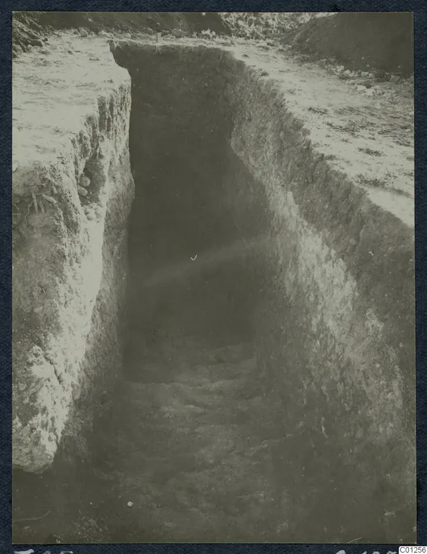 Excavation of Tomb 25 at Marion: a deep stepped cutting in earth with grass and stones at the top edges.