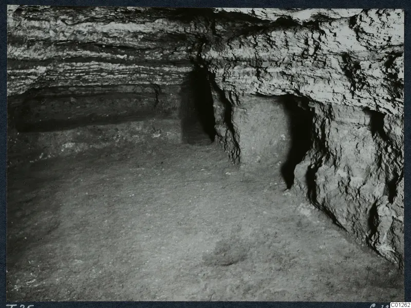 Interior of Tomb 25 at Marion, with layered rock walls, a recess in the right-hand wall and an earth floor