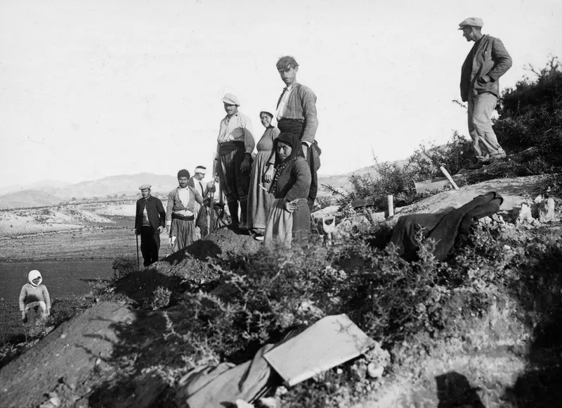 Workers and onlookers standing on a mound of excavated earth at Marion, with low hills and shrubs behind