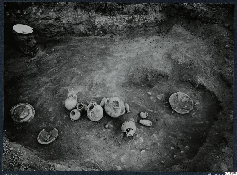 Tomb 50 at Marion during excavation, with pottery vessels and plates lying on the floor among scattered stones