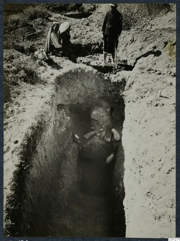 Tomb 56 at Marion during excavation, with two seated people and a standing man at the edge of the cut