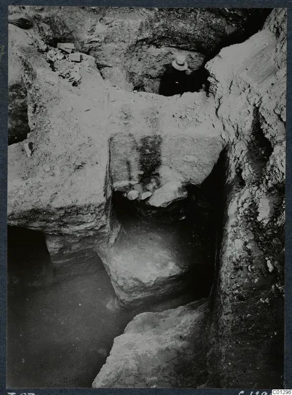 Excavation at Marion, Tomb 57, showing cut rock faces and a stepped cutting, with a person's hat visible at the top.