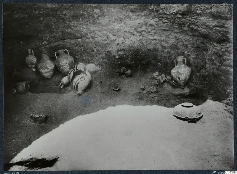 Handled pottery vessels and bowls lying on the floor of Tomb 58 at Marion during excavation.