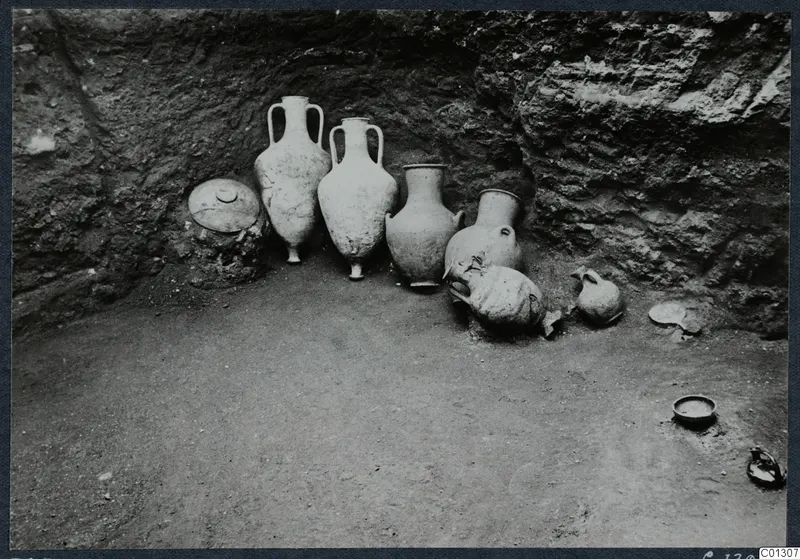 Tomb 57 at Marion during excavation, with a group of jars and bowls lying in place against a rock-cut wall