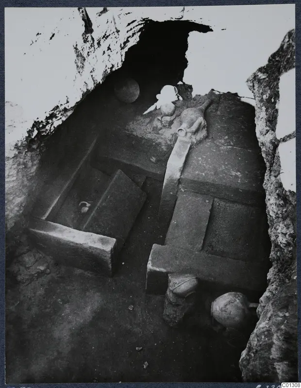 Interior of Tomb 53 at Marion, with stone slabs and several vessels inside a rock-cut chamber.