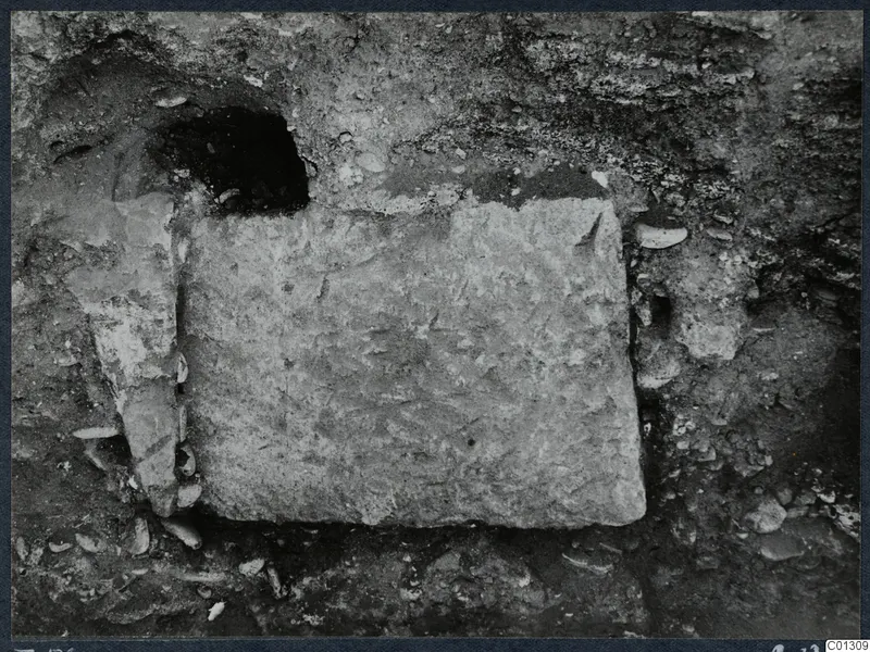 Tomb 59 at Marion: a large rectangular stone slab set in excavated soil, with a dark cavity above it and a smaller stone at left.
