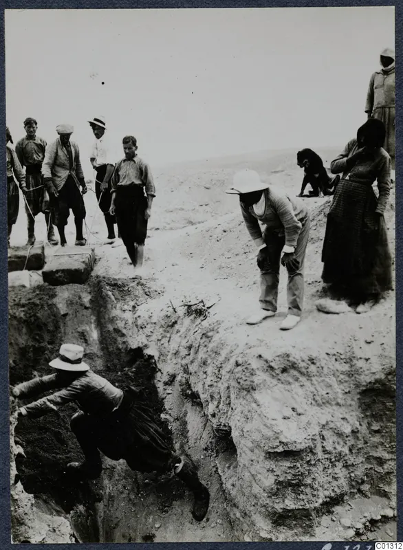 Workers and onlookers at the excavation of Tomb 53 at Marion, one man climbing down into a steep cut in the ground.