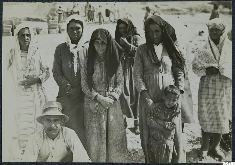 Group of women in headscarves and long dresses with a seated man and a small boy, at the excavation at Marion.