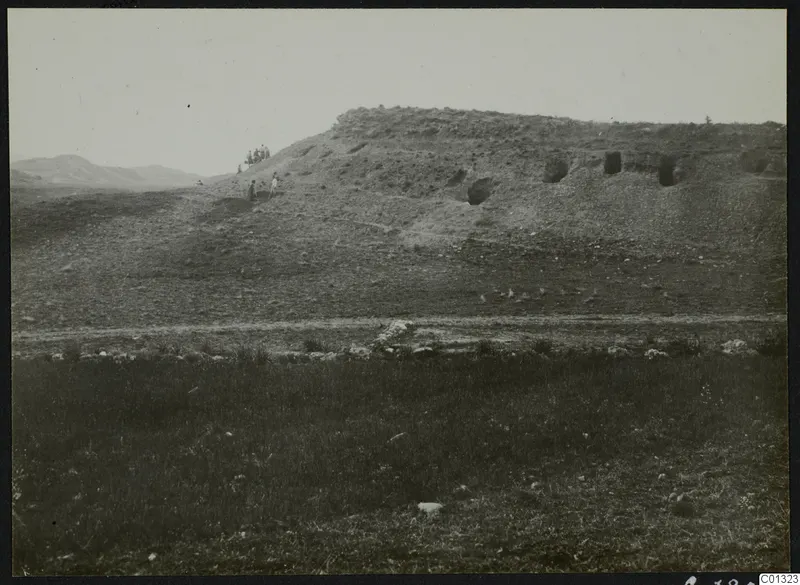 Eroded slope at Marion with dark openings cut into its face, a small group of people on the slope, and stones in the foreground.