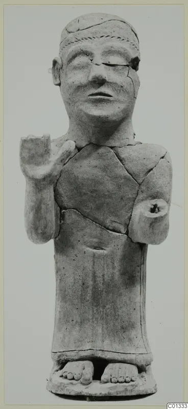 Terracotta statue of a standing human figure with one arm raised, shown cracked and repaired, against a plain background