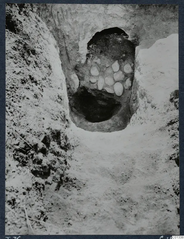 Tomb 76 at Marion during excavation, with a dark chamber opening framed by pale stones in the side of a trench.