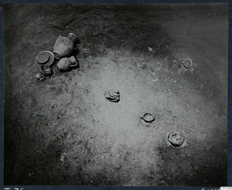 Excavated tomb floor at Marion with clay vessels, a shallow bowl and small rings lying in the soil