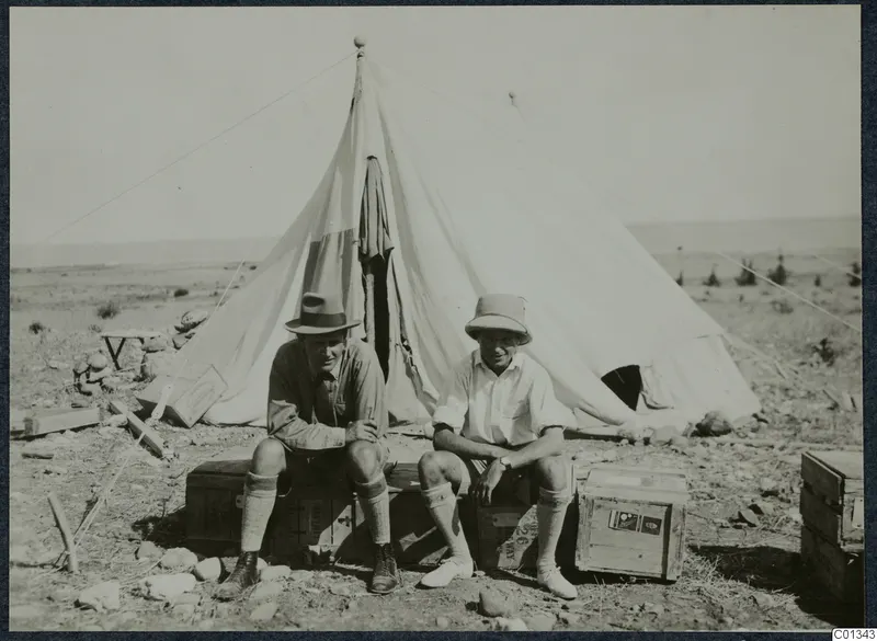 Two men sit on wooden crates outside a large white tent at Marion.
