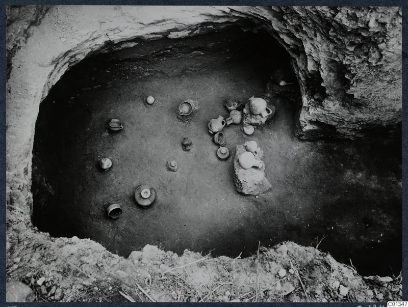Tomb 63 at Marion during excavation, with small clay vessels set on the floor of a rock-cut chamber