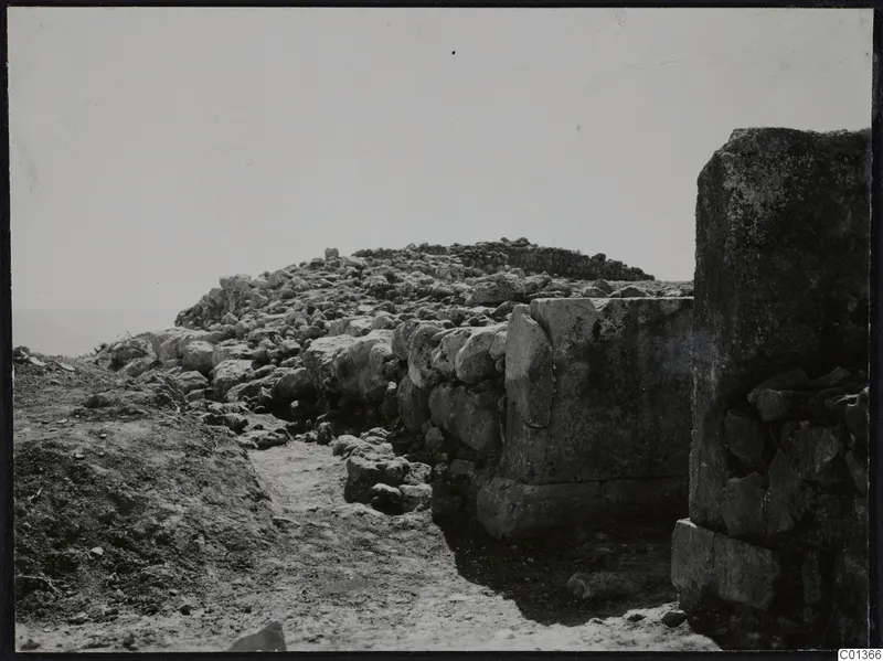 Nitovikla: loose stone rubble and a wall of large blocks at an excavation, with a tall upright stone at the right edge.