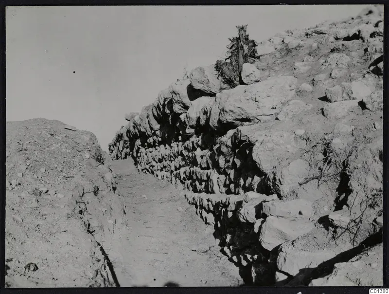 North enclosure wall at Nitovikla seen from the west, rough stone courses beside a dirt path