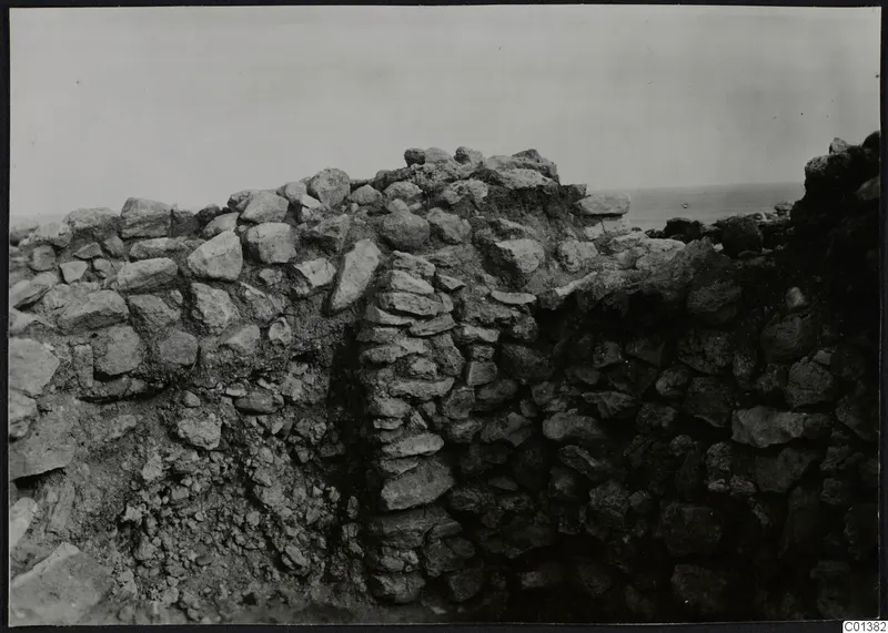 Stone wall foundations at Nitovikla, with sea visible on the horizon behind.