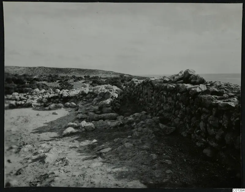 Stone wall and scattered rubble at Nitovikla, with low scrubby hills and the sea beyond