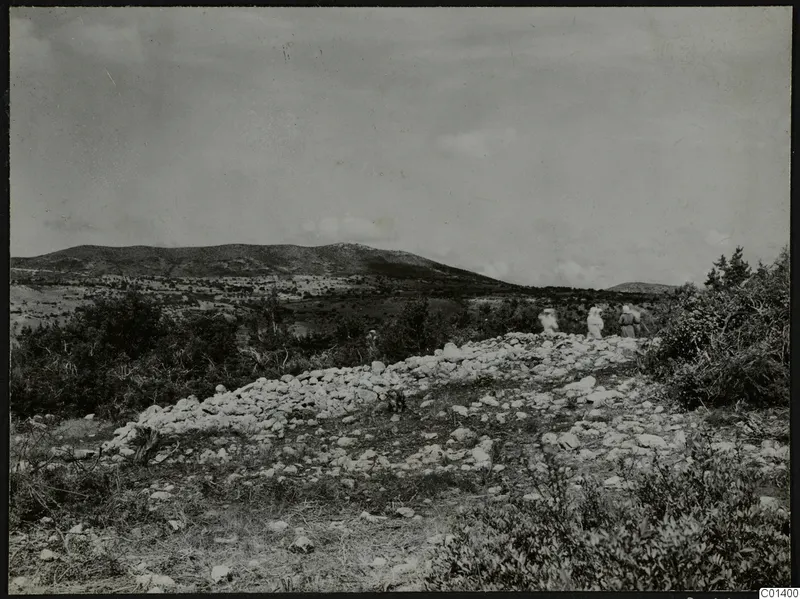 Nitovikla on the Karpas Peninsula: scattered pale stones and scrub in the foreground, low hills behind, with people standing at right.