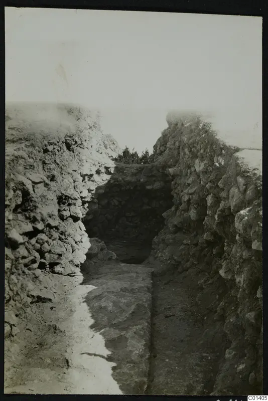 Excavated trench between rough stone walls, with a flat stone slab on the floor and a dark recess at the far end