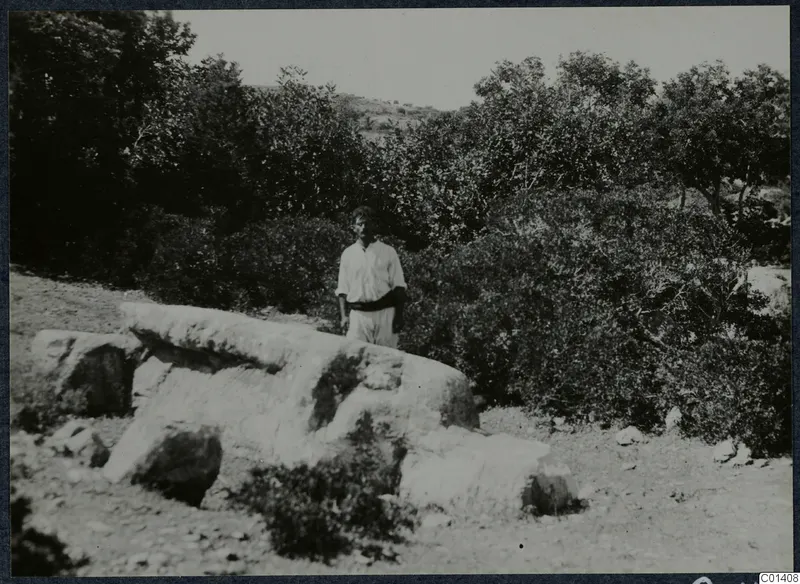 Man standing behind large pale stone blocks among scrub and trees on the Karpas peninsula.
