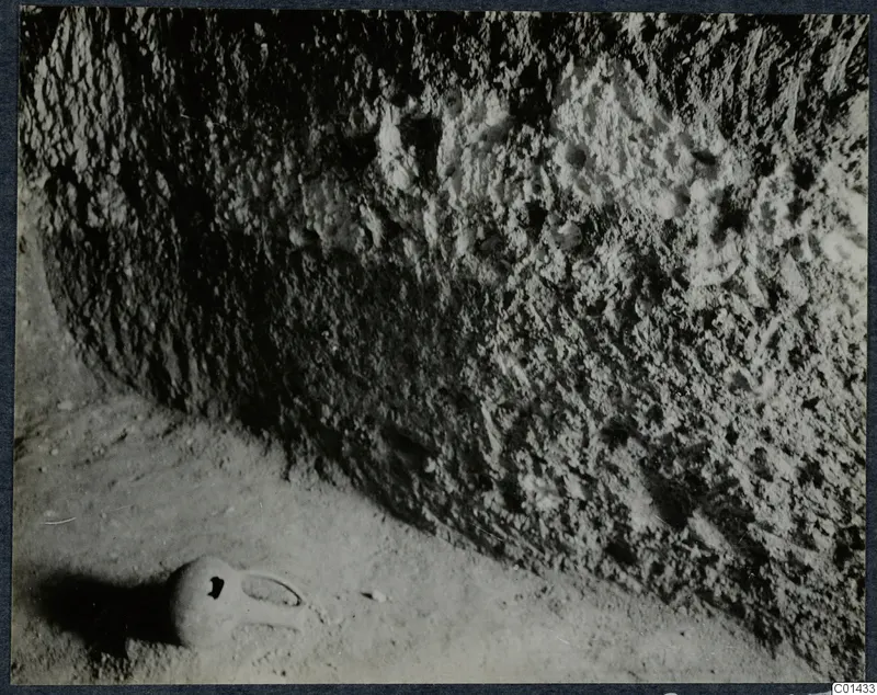 Rock-cut tomb wall at Ayios Iakovos with a small vessel lying on the floor in front of it