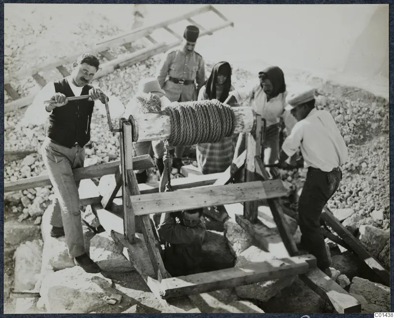 Men work a wooden windlass over a well at Vouni, lowering a man into the shaft