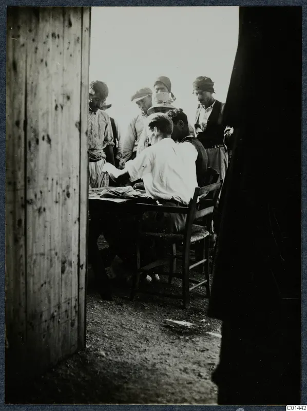 Payment at Vouni: a seated man at a table with papers, watched by standing men in caps and headscarves.